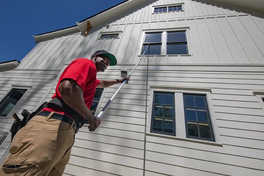 A technician using a long pole on the second-floor windows of a white house