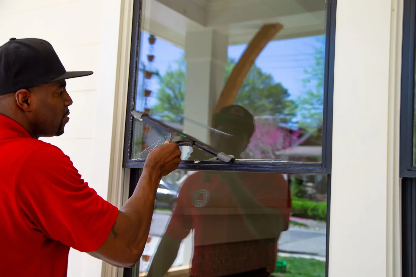 Close-up of a squeegee pulled across a window pane with trees reflected in the glass
